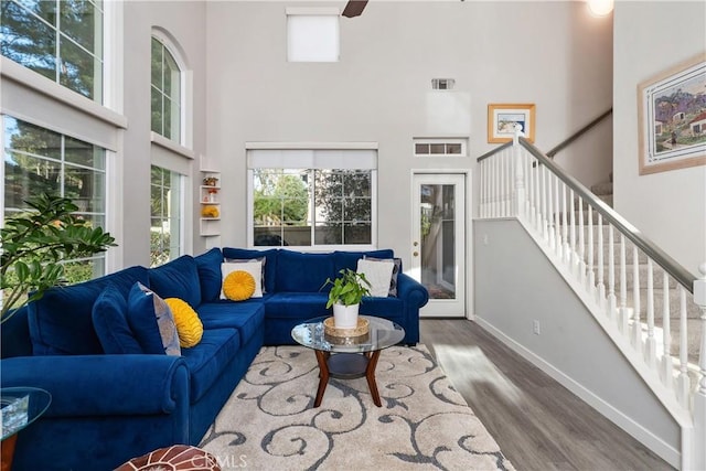 living room featuring baseboards, visible vents, wood finished floors, stairs, and a high ceiling