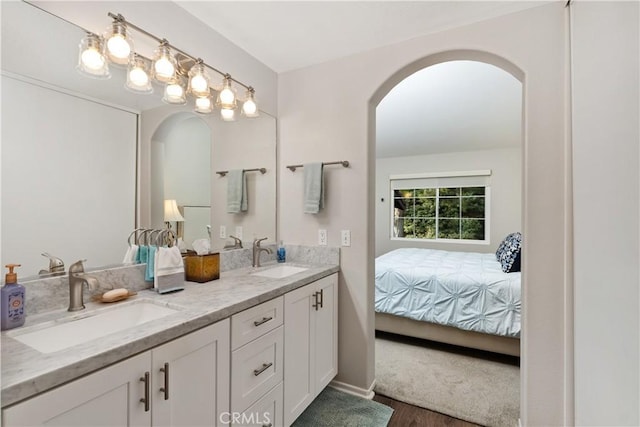 ensuite bathroom with double vanity, ensuite bath, a sink, and wood finished floors