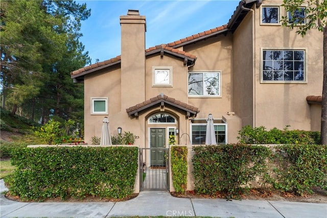 view of front of house featuring a fenced front yard, a chimney, a tiled roof, a gate, and stucco siding