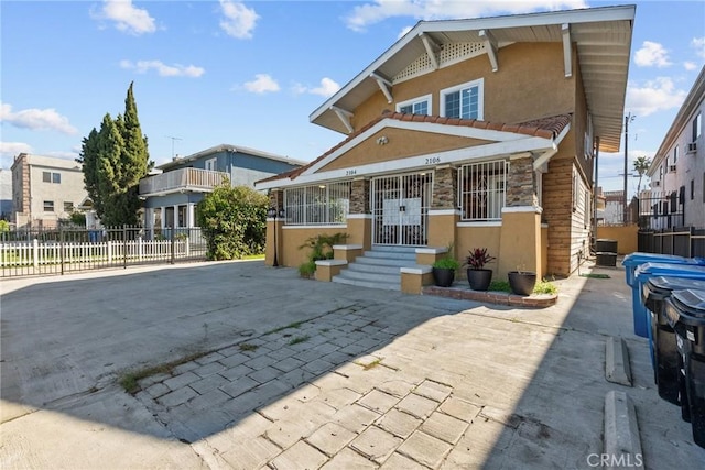 view of front of house with fence, a tiled roof, stucco siding, stone siding, and central air condition unit