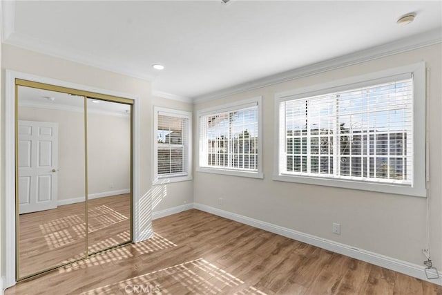 unfurnished bedroom with crown molding, baseboards, recessed lighting, wood finished floors, and a closet