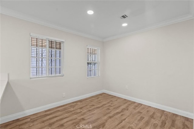 spare room with wood finished floors, visible vents, baseboards, and ornamental molding