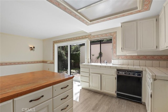 kitchen featuring tile countertops, light wood finished floors, a sink, dishwasher, and a peninsula