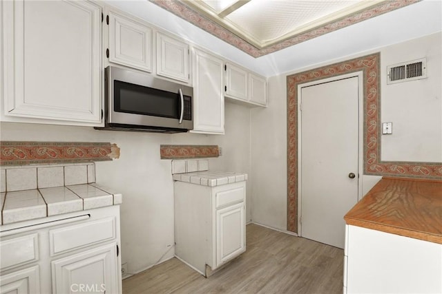 kitchen featuring light wood-style flooring, visible vents, white cabinetry, tile counters, and stainless steel microwave