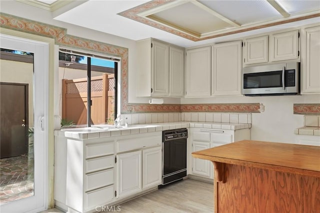 kitchen with light wood finished floors, black dishwasher, stainless steel microwave, and a sink