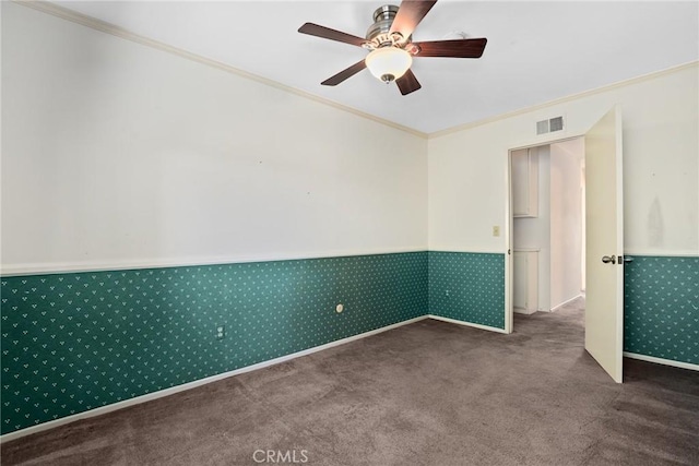 empty room with carpet floors, a wainscoted wall, ornamental molding, and visible vents