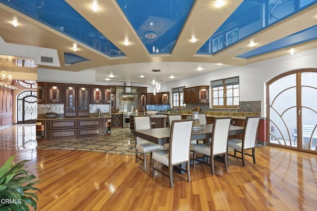 dining area featuring a towering ceiling, light wood-style flooring, visible vents, and beverage cooler