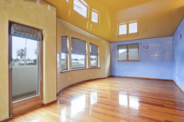 empty room with a high ceiling, baseboards, and wood finished floors