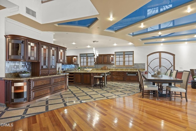 kitchen with visible vents, dark brown cabinets, light wood finished floors, a kitchen bar, and glass insert cabinets