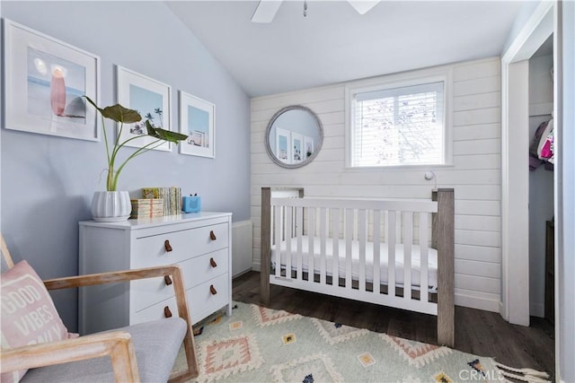 bedroom with ceiling fan, lofted ceiling, wooden walls, wood finished floors, and a nursery area