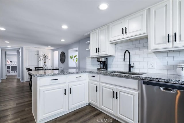 kitchen featuring dark wood-style floors, a peninsula, stainless steel dishwasher, white cabinetry, and a sink