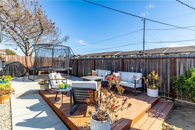 deck with a trampoline, a fenced backyard, and an outdoor living space