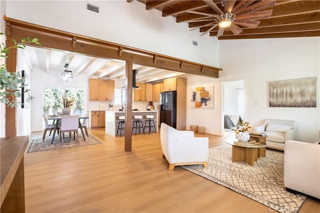 living room with beamed ceiling, visible vents, and light wood-style floors