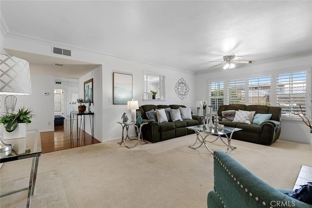 living room featuring visible vents, crown molding, carpet flooring, and ceiling fan