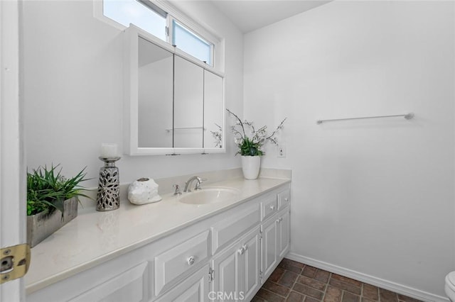 bathroom featuring stone finish flooring, toilet, vanity, and baseboards