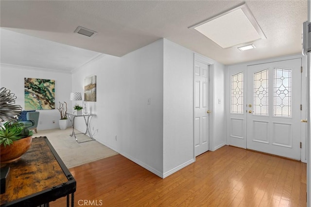 foyer entrance with a textured ceiling, visible vents, light wood-style flooring, and baseboards