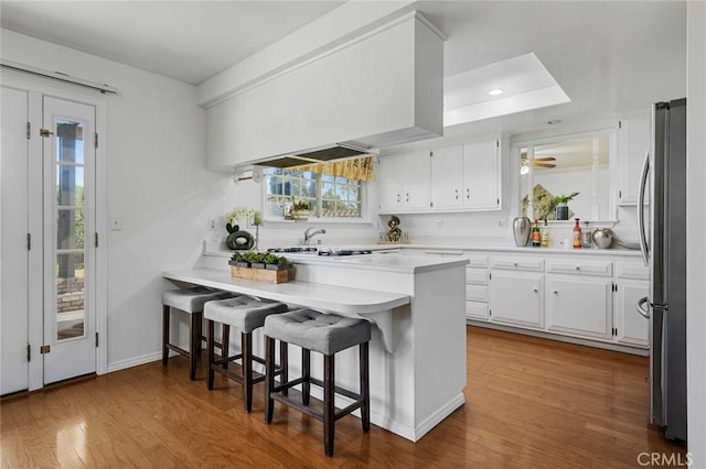 kitchen with a peninsula, wood finished floors, freestanding refrigerator, and white cabinetry