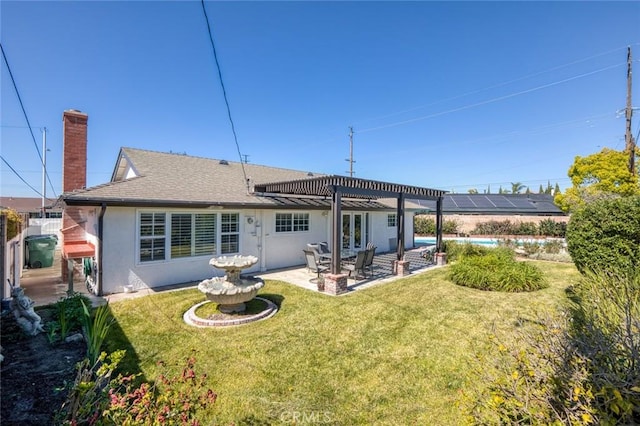 back of property with a patio, a shingled roof, a yard, stucco siding, and a chimney