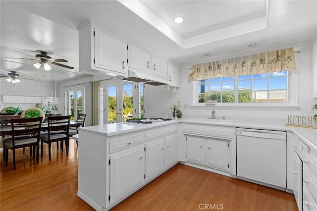 kitchen featuring white appliances, light wood-style flooring, a peninsula, french doors, and a sink