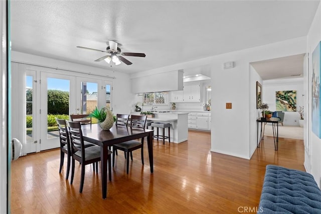 dining space featuring light wood-style floors, french doors, ceiling fan, and a textured ceiling