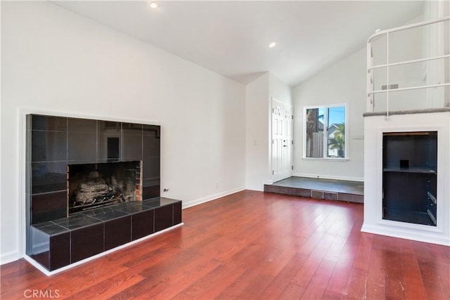 unfurnished living room with high vaulted ceiling, a tile fireplace, recessed lighting, wood finished floors, and baseboards