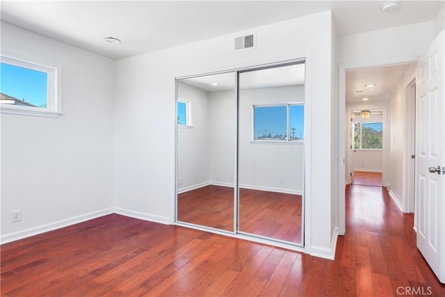 unfurnished bedroom featuring wood-type flooring, a closet, visible vents, and baseboards