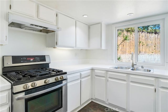 kitchen featuring under cabinet range hood, a sink, white cabinets, light countertops, and stainless steel range with gas stovetop