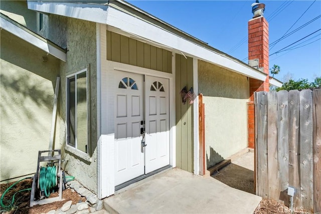 property entrance featuring fence, a chimney, and stucco siding