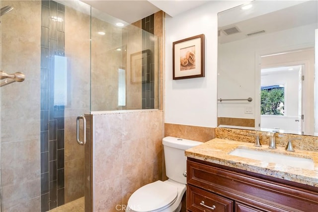 full bathroom with a stall shower, visible vents, toilet, vanity, and tile walls