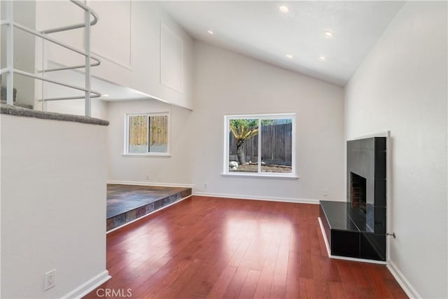 unfurnished living room featuring high vaulted ceiling, baseboards, a fireplace with raised hearth, and hardwood / wood-style floors