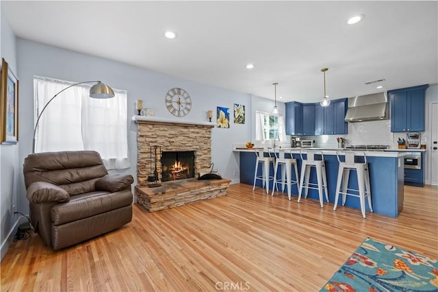 living room with a stone fireplace, light wood-style flooring, and recessed lighting