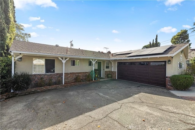 single story home featuring roof mounted solar panels, brick siding, an attached garage, and stucco siding