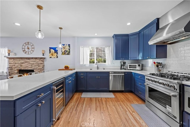 kitchen with appliances with stainless steel finishes, a sink, blue cabinets, a peninsula, and wall chimney exhaust hood