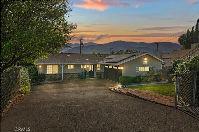 single story home with stucco siding, roof mounted solar panels, a mountain view, fence, and a garage