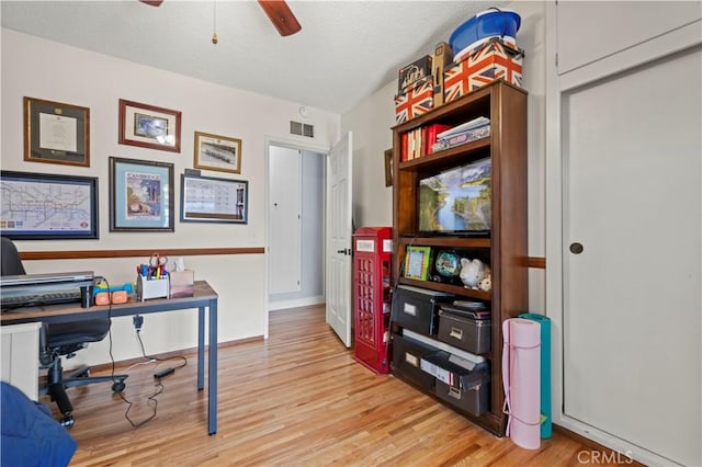 office featuring a textured ceiling, a ceiling fan, baseboards, visible vents, and light wood-style floors