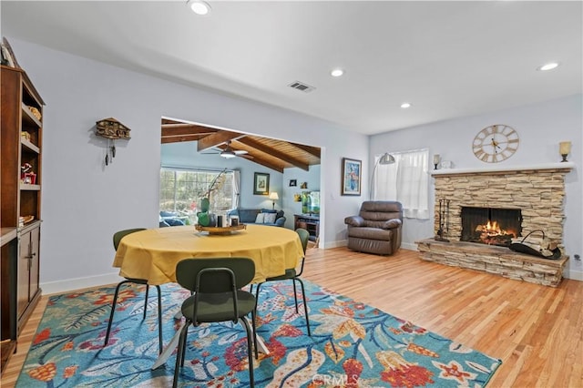 dining area featuring vaulted ceiling with beams, a stone fireplace, wood finished floors, visible vents, and baseboards