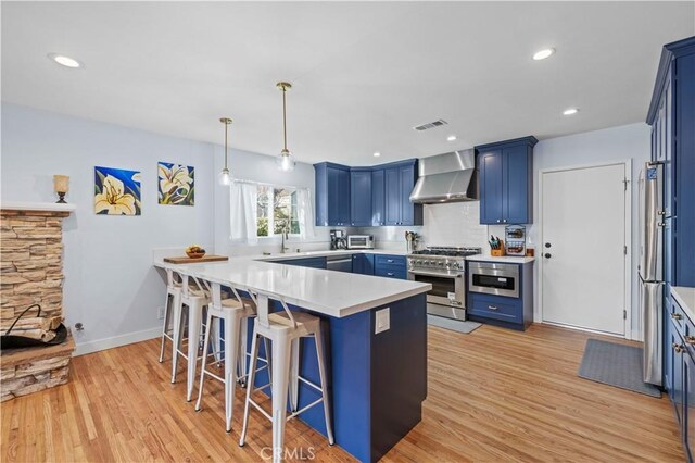 kitchen featuring blue cabinetry, visible vents, appliances with stainless steel finishes, wall chimney range hood, and a kitchen breakfast bar