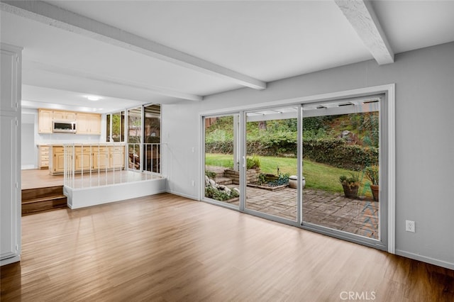 unfurnished living room with beamed ceiling, baseboards, and light wood-type flooring