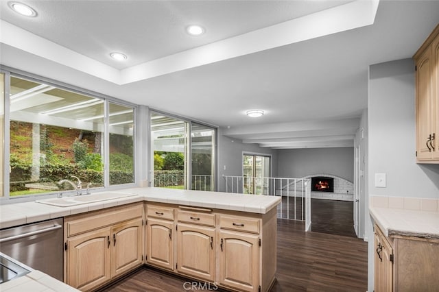 kitchen with tile countertops, a brick fireplace, dark wood-type flooring, and a sink