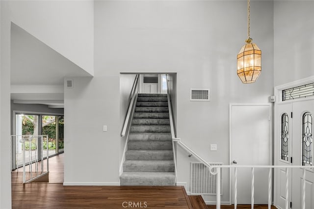 entrance foyer with visible vents, wood finished floors, a towering ceiling, and stairway