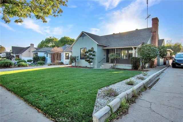 ranch-style house with a shingled roof, a chimney, a front yard, and stucco siding