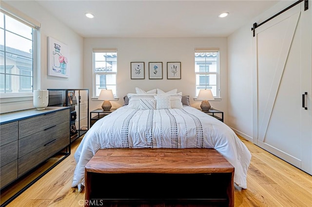 bedroom with recessed lighting, a barn door, and light wood finished floors