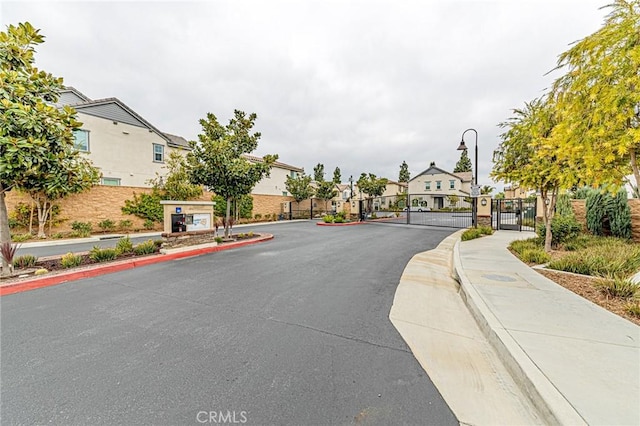 view of street with a gate, sidewalks, street lighting, a gated entry, and a residential view