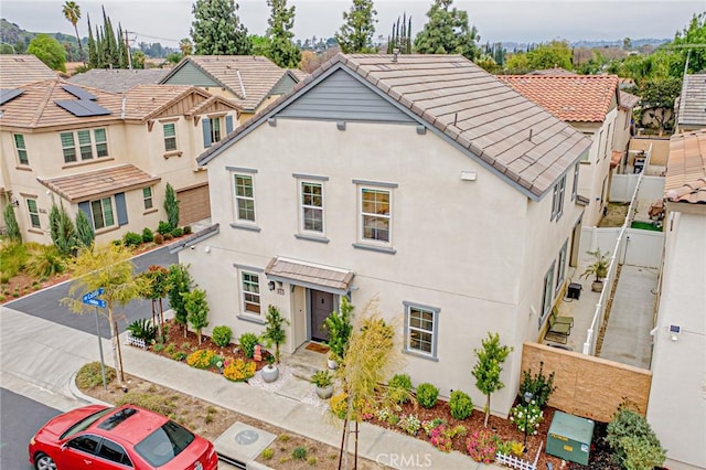 view of front facade featuring fence, a residential view, a tile roof, stucco siding, and driveway