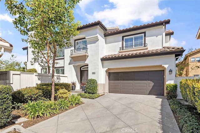 mediterranean / spanish-style house with concrete driveway, a tiled roof, an attached garage, fence, and stucco siding