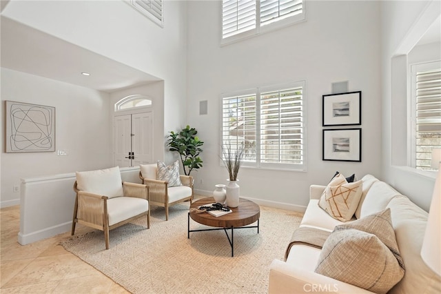 living room featuring a healthy amount of sunlight, light tile patterned floors, a high ceiling, and baseboards