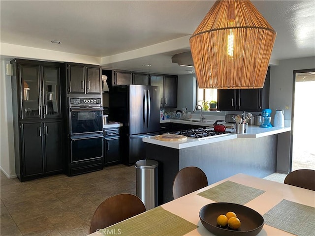 kitchen with dobule oven black, freestanding refrigerator, a peninsula, light countertops, and a sink