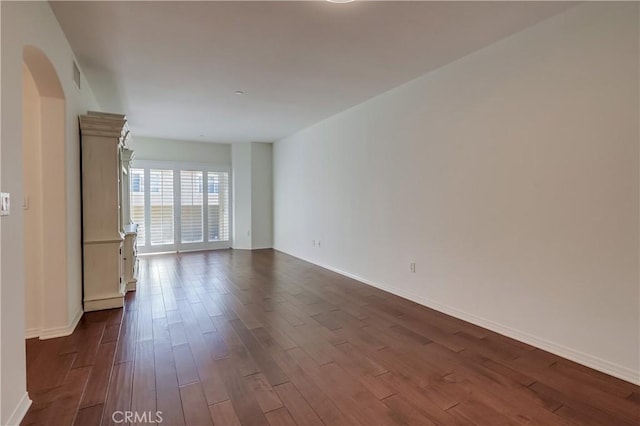 spare room with arched walkways, visible vents, dark wood finished floors, and baseboards