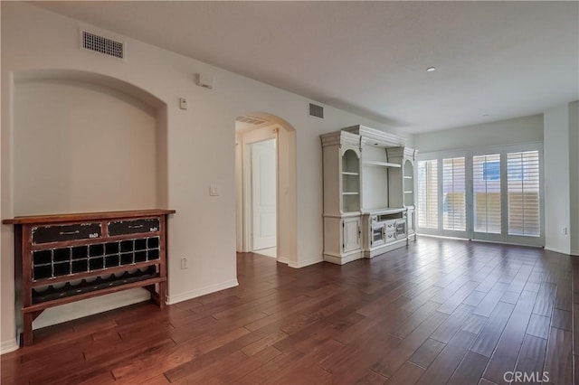 unfurnished living room featuring arched walkways, dark wood-style flooring, visible vents, and baseboards