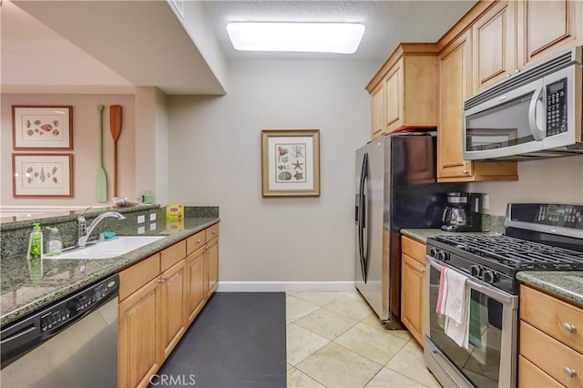 kitchen featuring stainless steel appliances, light tile patterned flooring, a sink, light brown cabinets, and dark stone countertops